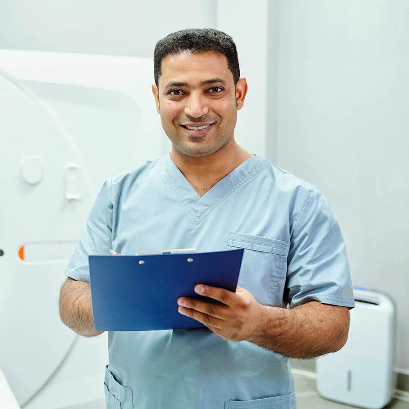 A healthcare student stands beside a CAT Scan machine